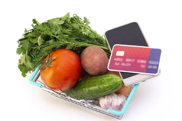 ordering food at home in connection with isolation from the coronavirus. phone and card. a person places an order. tomato, cucumber, greens in a basket.