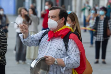 Coruna-İspanya. 19 Mayıs 2020 'deki covid-19 salgını sırasında İspanya hükümetine karşı yüz maskeli protestocu bir tencereye dokundu.