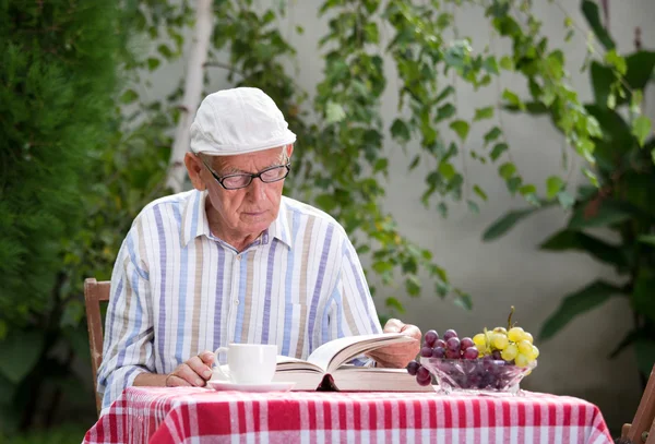 Senior man läser bok i trädgården — Stockfoto