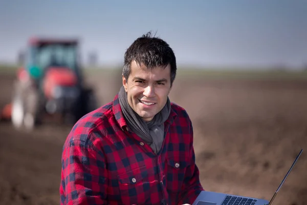 Famer met laptop en trekker in veld — Stockfoto