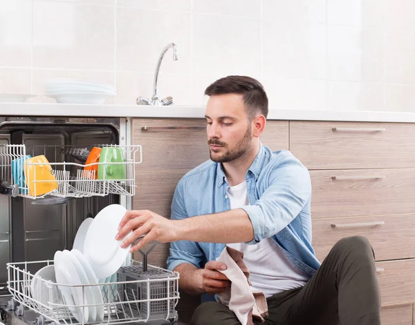 Человек разгружает посудомоечную машину — стоковое фото