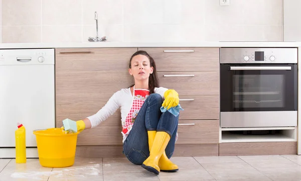 Femme de ménage fatiguée assise sur le sol de la cuisine — Photo