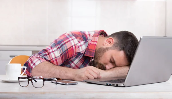Человек спит над ноутбуком дома — стоковое фото