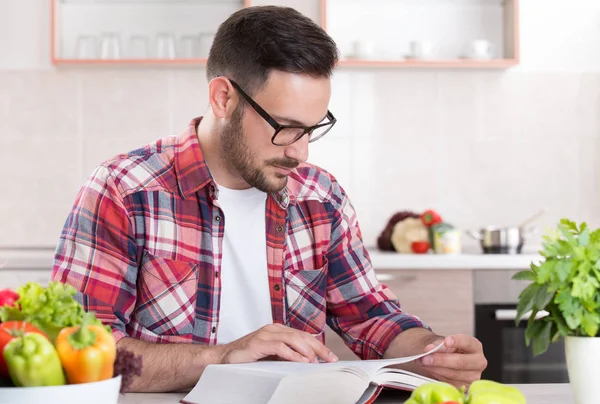 Homem leitura livro de receitas na cozinha — Fotografia de Stock