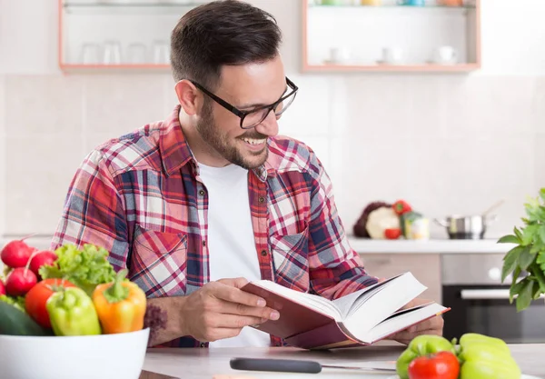 Homem leitura livro de receitas na cozinha — Fotografia de Stock