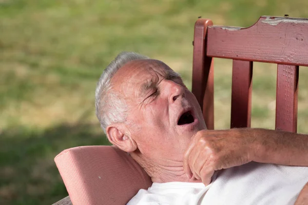 Senior gähnt im Garten auf Bank — Stockfoto