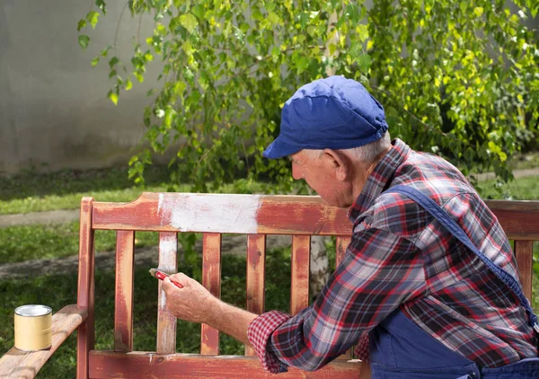 Old man painting bench in garden — Stock Photo, Image