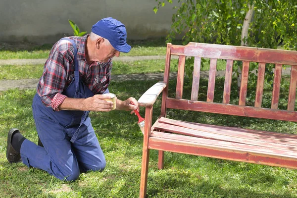Starý muž malba lavička v zahradě — Stock fotografie