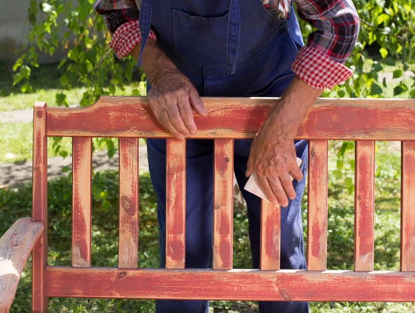 Old man sandblasting bench in garden — Stock Photo, Image