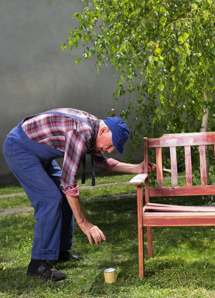 Старик рисует скамейку в саду — стоковое фото