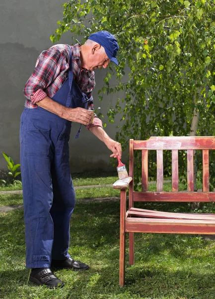 Old man painting bench in garden — Stock Photo, Image