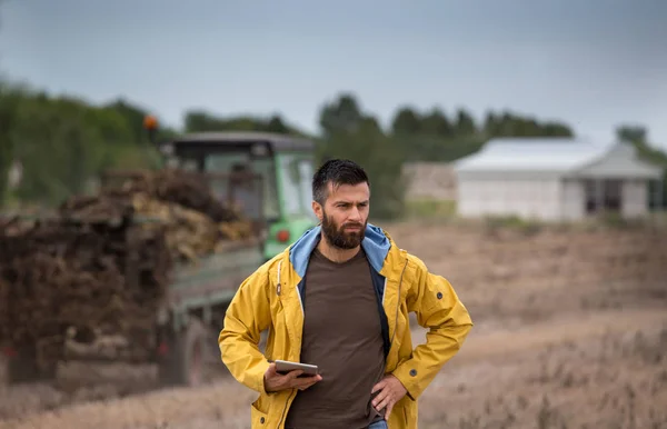 Farmer holding tablet with tractor behind — Stock Photo, Image