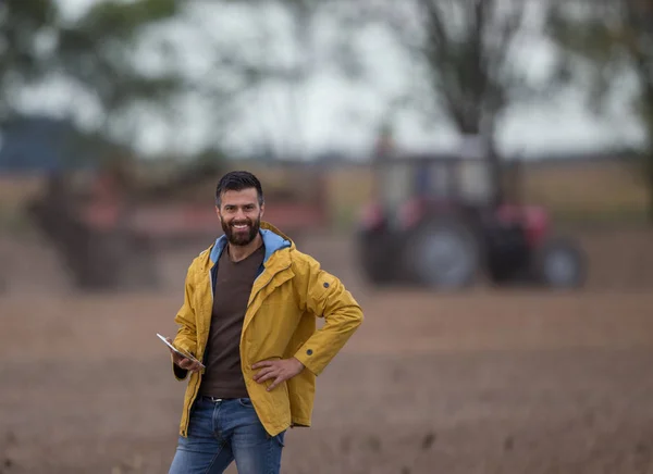 Farmer tenant tablette avec tracteur derrière — Photo