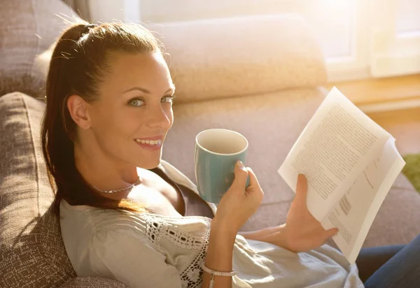 Dziewczyna, czytanie książki i picie kawy na kanapie — Zdjęcie stockowe