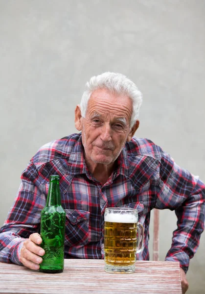 Homme âgé avec bouteille de bière et tasse — Photo