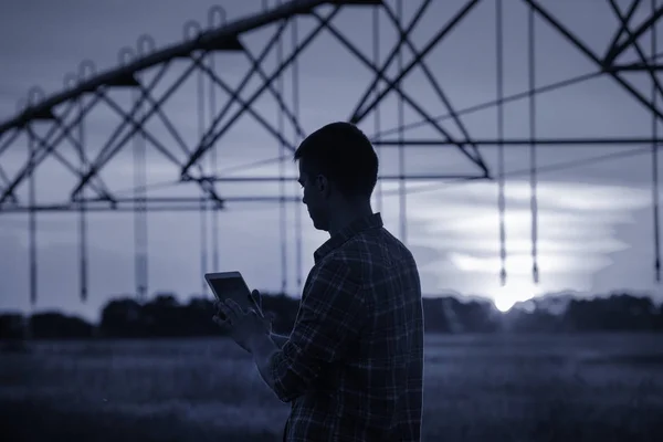 Farmer with tablet in front of irrigation system — Stock Photo, Image