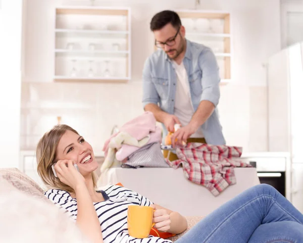 Hombre planchando mientras mujer descansando y hablando por teléfono — Foto de Stock