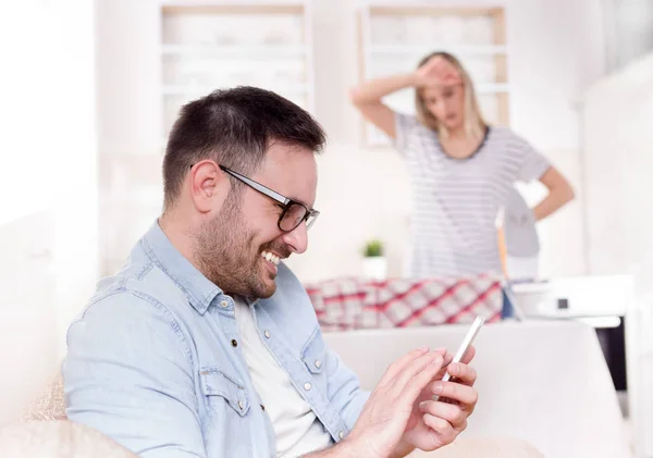 Marido descansando no sofá enquanto esposa fazendo tarefas — Fotografia de Stock