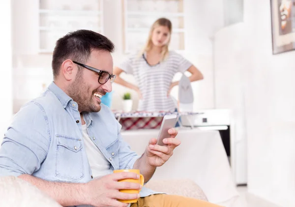 Marido descansando no sofá enquanto esposa fazendo tarefas — Fotografia de Stock