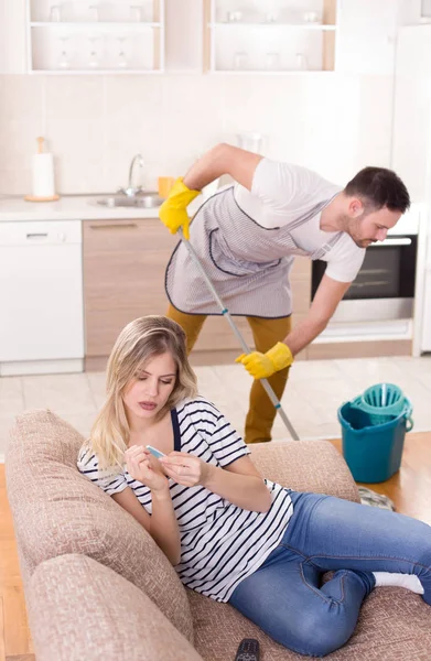 Uomo che pulisce il pavimento mentre la donna riposa sul divano — Foto Stock