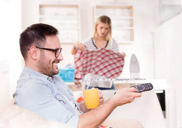 Hombre viendo televisión y mujer haciendo quehaceres domésticos —  Fotos de Stock