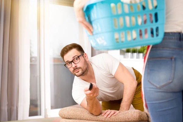 Женщина делает работу по дому, пока мужчина смотрит телевизор — стоковое фото