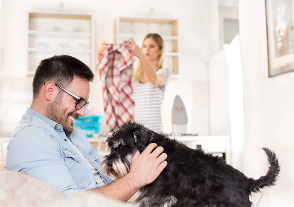 Uomo che gioca con cane e donna che fanno i lavori domestici — Foto Stock