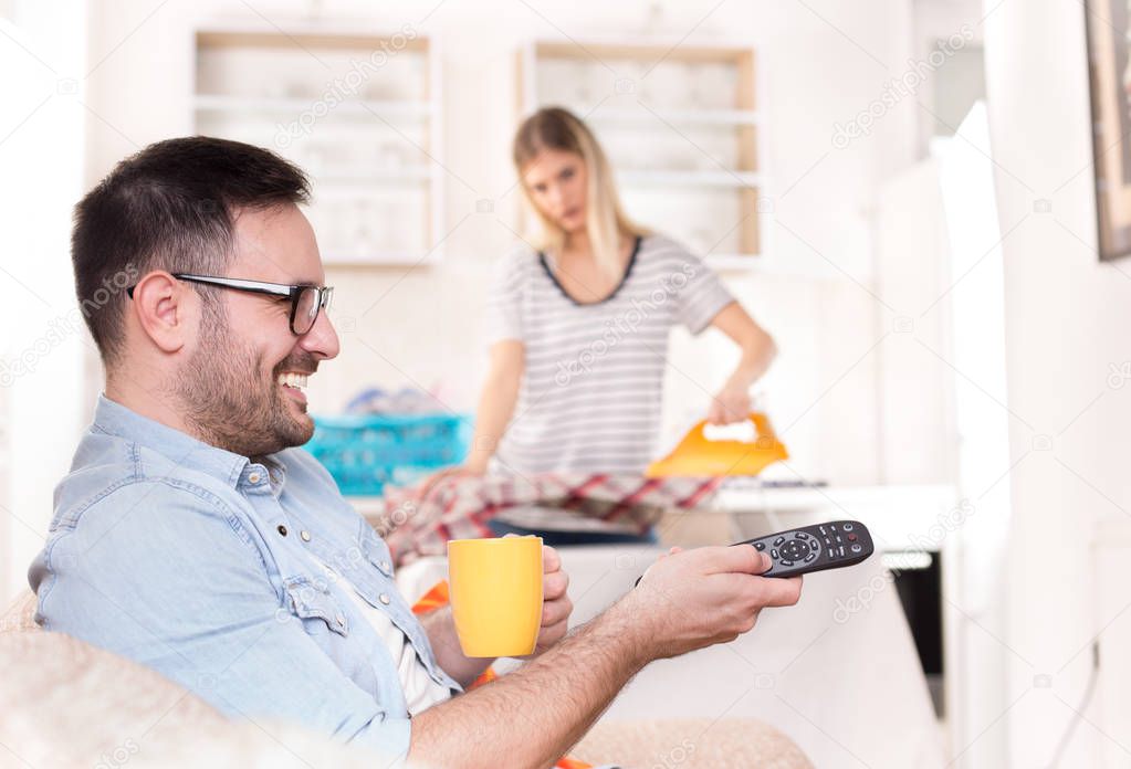 Man watching tv and woman doing housework