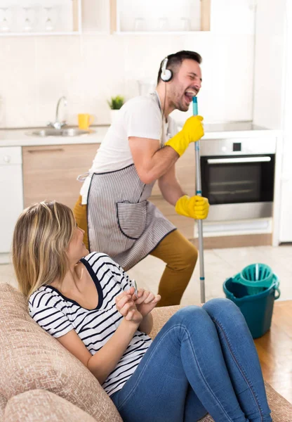 Uomo che pulisce il pavimento e canta alla ragazza sul divano — Foto Stock