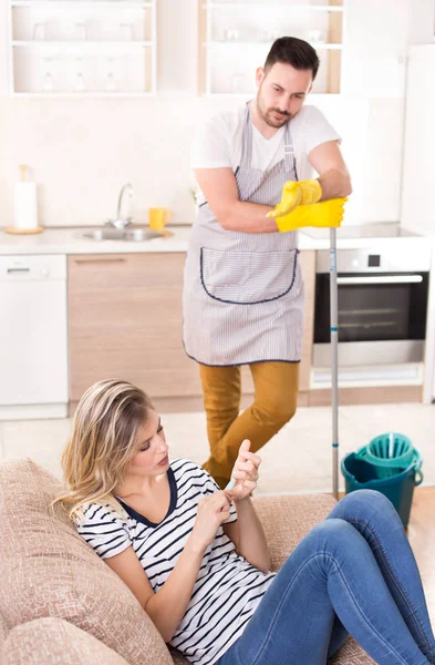 Uomo che pulisce il pavimento mentre la donna riposa sul divano — Foto Stock