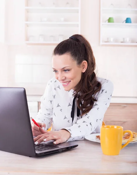 Smiling woman working on laptop in kitchen — Stock Photo, Image