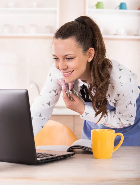Mulher com avental e pano trabalhando no laptop na cozinha — Fotografia de Stock