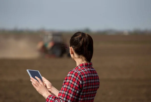 Mulher agricultor com tablet e trator em campo — Fotografia de Stock