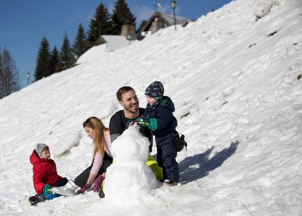 Szülők gyerekekkel hóembert csinálnak a hegyen — Stock Fotó