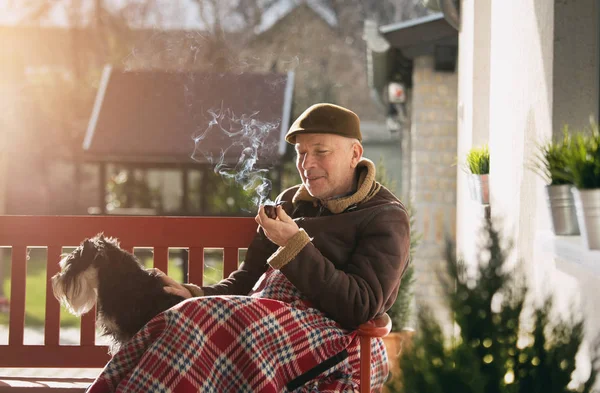 Alter Mann mit Hund auf Bank Pfeife rauchend — Stockfoto