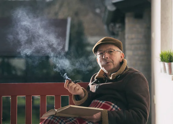 Stary człowiek pali fajkę i czyta książki w ogrodzie — Zdjęcie stockowe