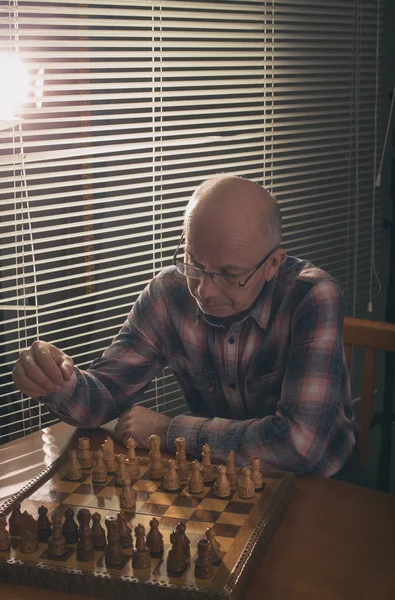 Homem jogando xadrez ao lado de janelas cortinas wtih — Fotografia de Stock