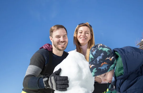 Eltern mit Junge basteln Schneemann am Berg — Stockfoto