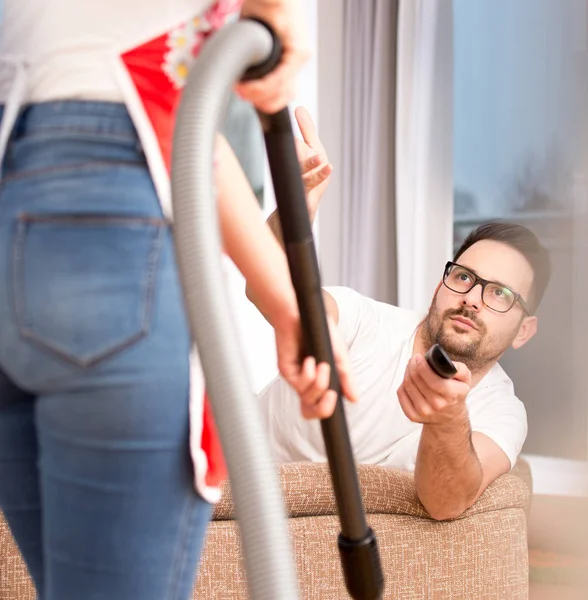 Woman vacuuming while man watching tv