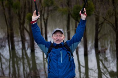 Heyecanlı yaşlı yürüyüşçü ormanda sopalarla kollarını kaldırıyor. Kişisel başarı ve başarı kavramı