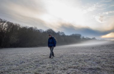 Soğuk ve sisli kış sabahında ormanda yürüyen sırt çantalı olgun bir yürüyüşçü.