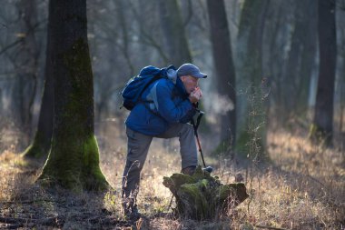 Olgun bir yürüyüşçü ağaca yaslanır ve ellerini ısıtarak onları ovuşturur ve soğuk kış sabahında sıcak hava üfler.