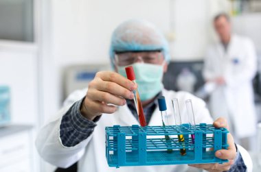 Laboratuvarda renkli sıvılarla test tüplerini tutan araştırmacının elini kapatın.