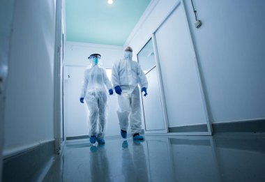 Laboratuvar koridorunda yürüyen koruyucu giysili araştırmacılar. Virüs ve hastalıklar güvenlik kavramı