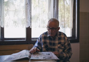 Gözlüklü son sınıf öğrencisi evdeki eski moda iç mekanlarda gazete okuyor.