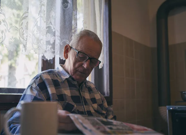 一个戴眼镜的老年人在家里的老式室内装潢的桌子边看报 — 图库照片