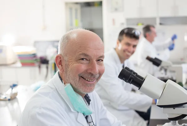 研究室の同僚と顕微鏡に取り組む上級生物学者の肖像 — ストック写真
