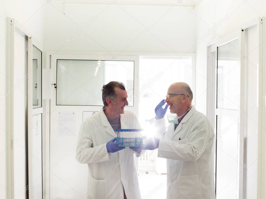 Two colleagues communicating and laughing while holding samples in test tubes in laboratory