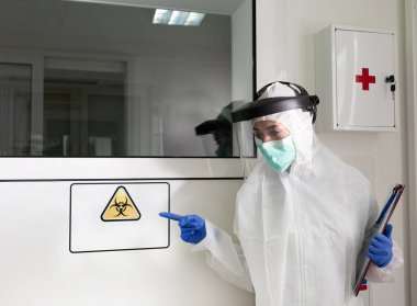 Koruyucu giysili ve güvenlik maskeli kadın laboratuvarda biyolojik tehlike işareti gösteriyor.