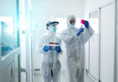 Koruyucu giysiler içindeki iki biyolog laboratuvar koridorunda numune taşıyor.